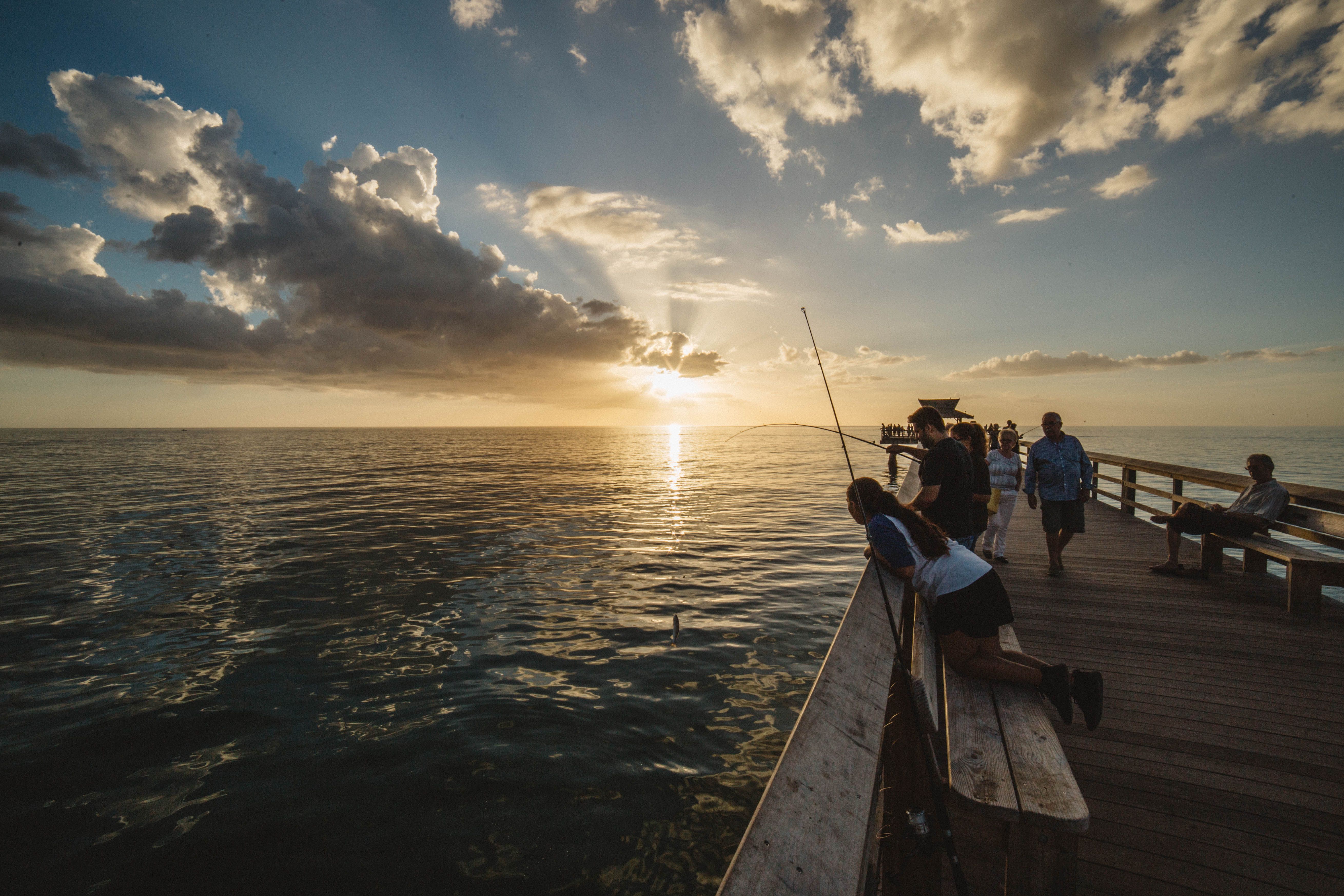 People fishing off a pier at sunset with ocean views